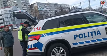 A Moldovan police officer standing by a patrol car on a city street.