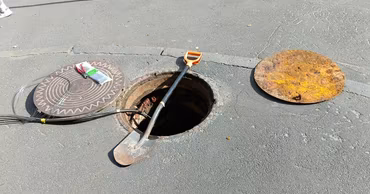 An open manhole cover on an asphalt road with a shovel resting inside.