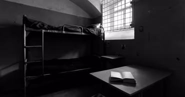 A black and white photo of a sparse prison cell with bunk beds.