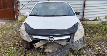 A damaged white Opel Corsa car parked on the side of the road.
