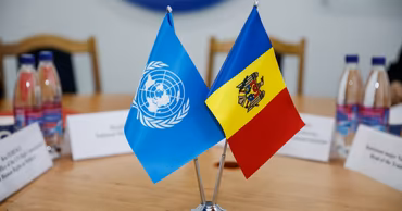 Flags of the United Nations and Moldova placed on a table during a diplomatic meeting.