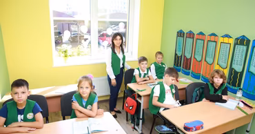 A teacher and several children wearing green vests sitting in a classroom.