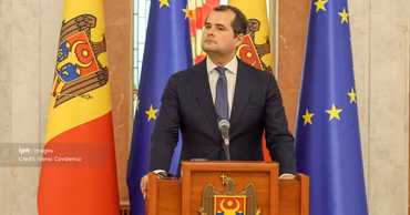 Vasile Tofan standing at a podium with Moldovan and European Union flags in the background.