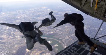Military paratroopers jumping from the open cargo door of a transport aircraft.