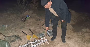 An environmental inspector points at confiscated fish and electrofishing equipment on the riverbank.