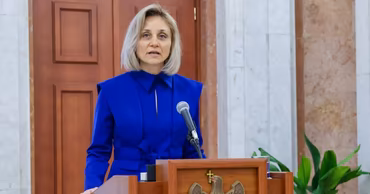 Tatiana Nistorică speaking at a podium with the Moldovan coat of arms.