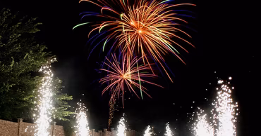 A car driving on a path lined with pyrotechnic fountains under a fireworks display.