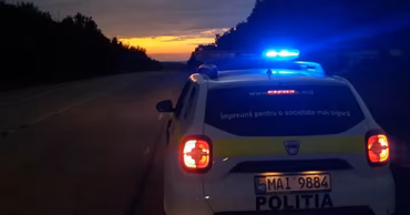 A Moldovan police car with flashing lights parked on a road at sunset.