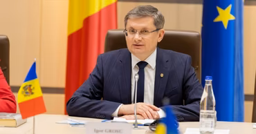Igor Grosu sitting at a table with Moldovan and EU flags in the background.
