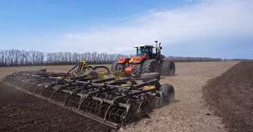 A large red tractor pulling a cultivator across a field during agricultural work.