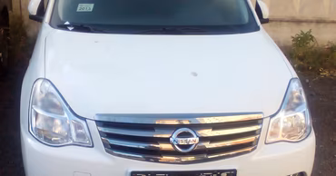 A white Nissan car parked in front of a concrete wall.