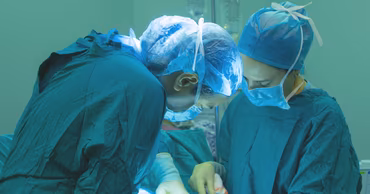 Two surgeons in scrubs and masks performing a surgical procedure in an operating room.