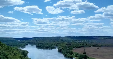 A scenic view of the Dniester River flowing through a green landscape under a cloudy sky.