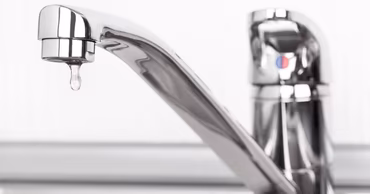 A close-up of a chrome water faucet with a single drop of water falling.