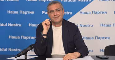 Renato Usatii sitting at a table with a microphone in front of a party banner.