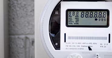 A close-up view of a modern digital smart electricity meter mounted on a wall.