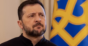 Ukrainian President Volodymyr Zelensky standing in front of a Ukrainian flag.