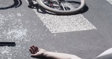A person lying on the asphalt next to a bicycle and broken glass.