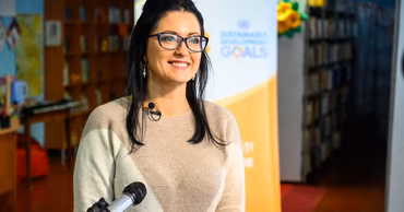 Natalia Plugaru speaking into a microphone in front of a Sustainable Development Goals banner.
