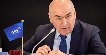 Ilie Bolojan speaking at a conference with an EPP flag on the table.