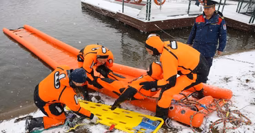 Moldovan GIGS rescuers in orange suits performing a water rescue operation in winter conditions.