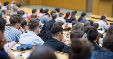 A crowded university lecture hall with students sitting at desks during a class.