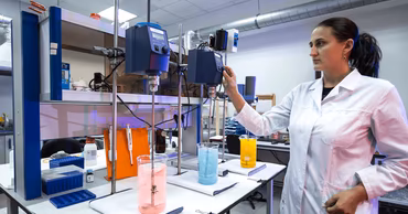 A female scientist in a laboratory coat working with chemical equipment and beakers.