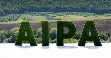 Large green letters spelling AIPA standing outdoors against a rural landscape background.