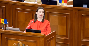 Liliana Vitu speaking at a podium in a formal setting with Moldovan flags.