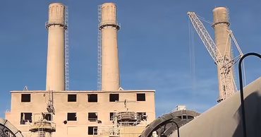 Industrial view of the Rîbnița Cement Plant with tall chimneys and construction equipment.