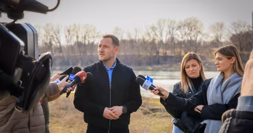 Gheorghe Hajder giving a press conference near a riverbank.