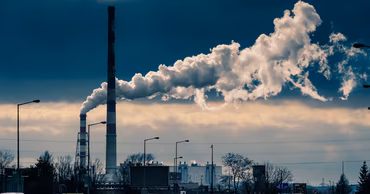 Industrial chimneys emitting smoke over a road with traffic in an urban environment.
