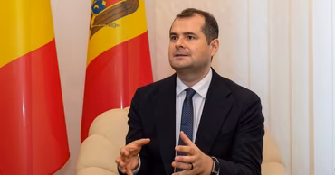 Vasile Tofan speaking in front of a Moldovan flag.