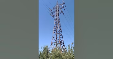 A high-voltage power line pylon standing in a field against a clear blue sky.