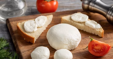 Mozzarella cheese balls on a wooden cutting board with bread and tomatoes.