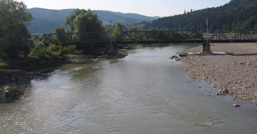 A river flowing under a metal bridge with exposed rocky banks indicating low water levels.