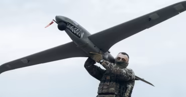 A soldier in camouflage holding a military drone with shark teeth markings.