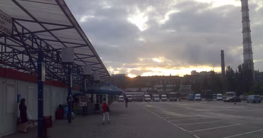 A view of a bus station in Chisinau with parked minibuses and passengers under a cloudy sky.