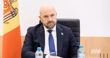 Andrei Spînu sitting at a table with the Moldovan flag in the background.