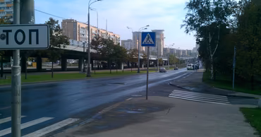 A city street with a pedestrian crossing and apartment buildings in the background.