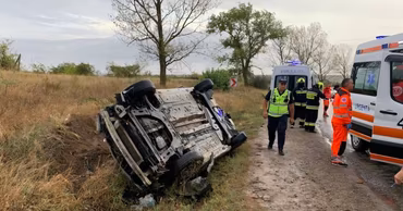 A car overturned on the side of a road with emergency services and an ambulance present.