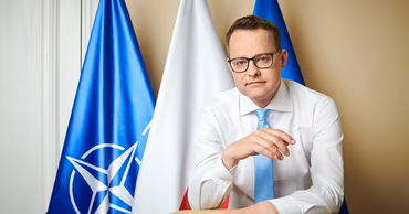 Marcin Romanowski posing in front of Polish and NATO flags.