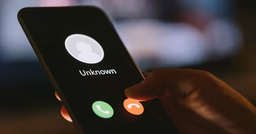 A hand holding a smartphone showing an incoming call from an unknown number.