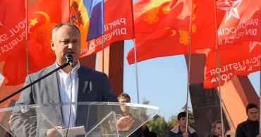 Igor Dodon speaking at a podium with PSRM party flags in the background.