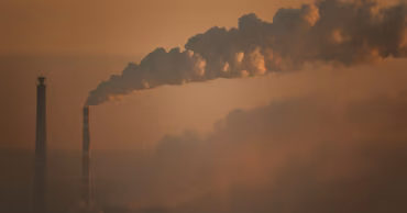 Industrial smokestacks emitting smoke into the air at sunset.