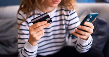 A person holding a bank card and a smartphone, illustrating online financial fraud.