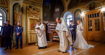 A bride and groom standing in an Orthodox church during a wedding ceremony with priests.