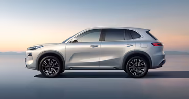 A side view of a silver Geely EX5 SUV against a sunset background.