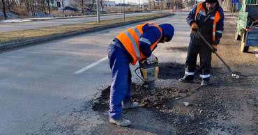Two construction workers in high-visibility vests repairing a road with a jackhammer.