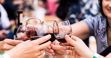 Close-up of several people toasting with glasses of red wine at an outdoor event.